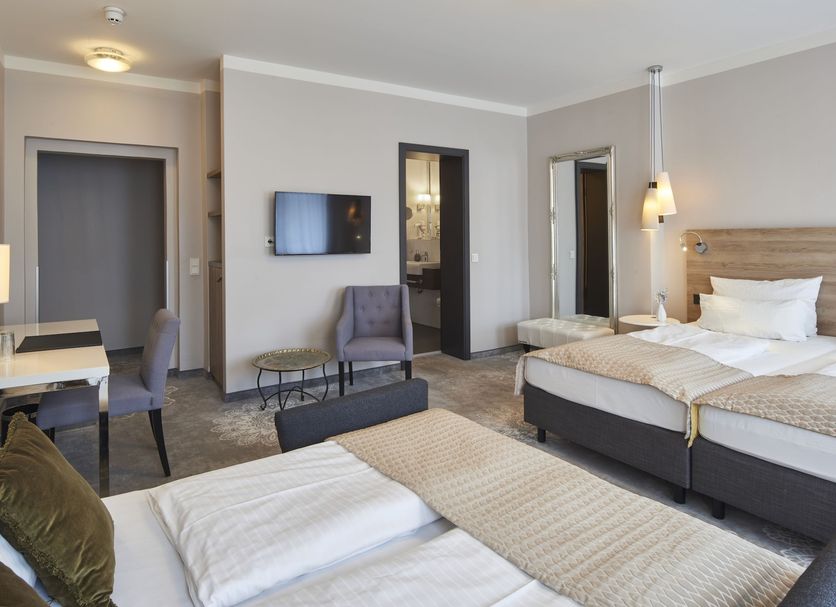 Hotel Via Regia in Görlitz: guest room with two beds, seating area and wall-mounted TV