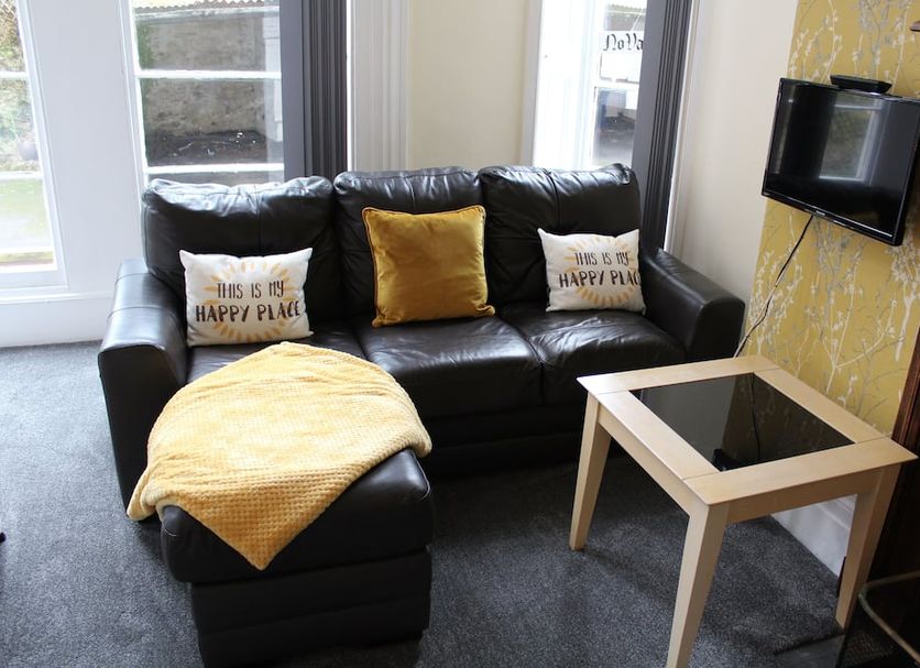 The Darnley Hotel, Ilfracombe: black leather sofa with yellow throw, side table and wall-mounted TV