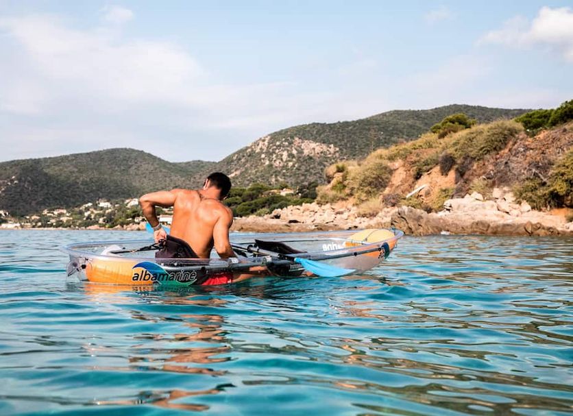 Hotel Stella Di Mare in Ajaccio overlooks a man kayaking on clear blue water near a rocky coastline.