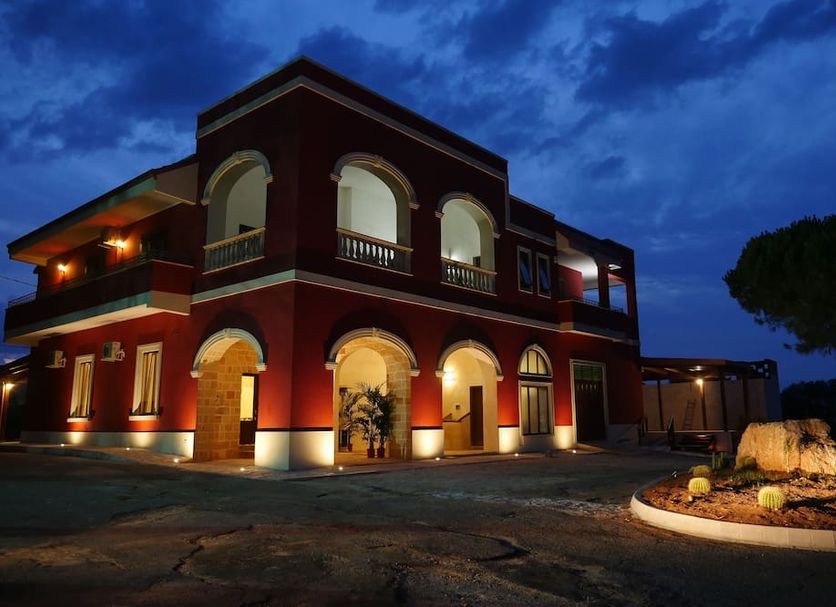 Tenuta Cavalieri in Leverano, illuminated red hotel exterior with arched windows and landscaped entrance