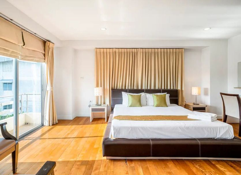 Nara Suite Residence Bangkok guest room with king bed, balcony doors, and bright wood flooring in Bangkok