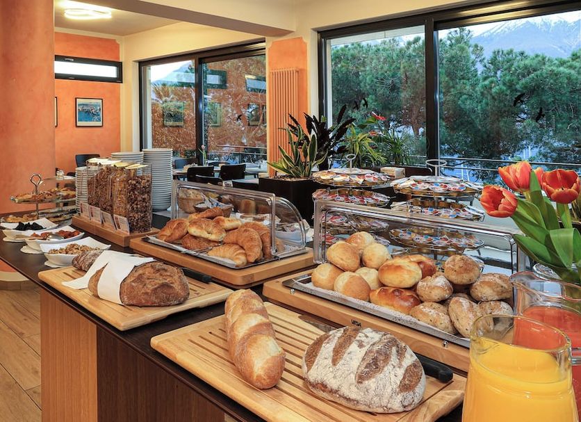 Breakfast buffet at Hotel Geranio Au Lac in Locarno with pastries, bread, and orange juice by large windows