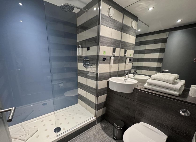 Village Hotel Glasgow in Glasgow bathroom with walk-in shower, sink, and stacked towels