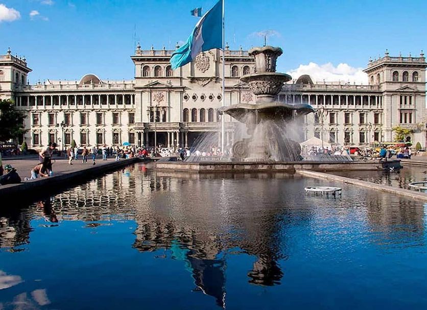 Hostal Villa Toscana in Guatemala City with a city fountain and historic building reflected in water