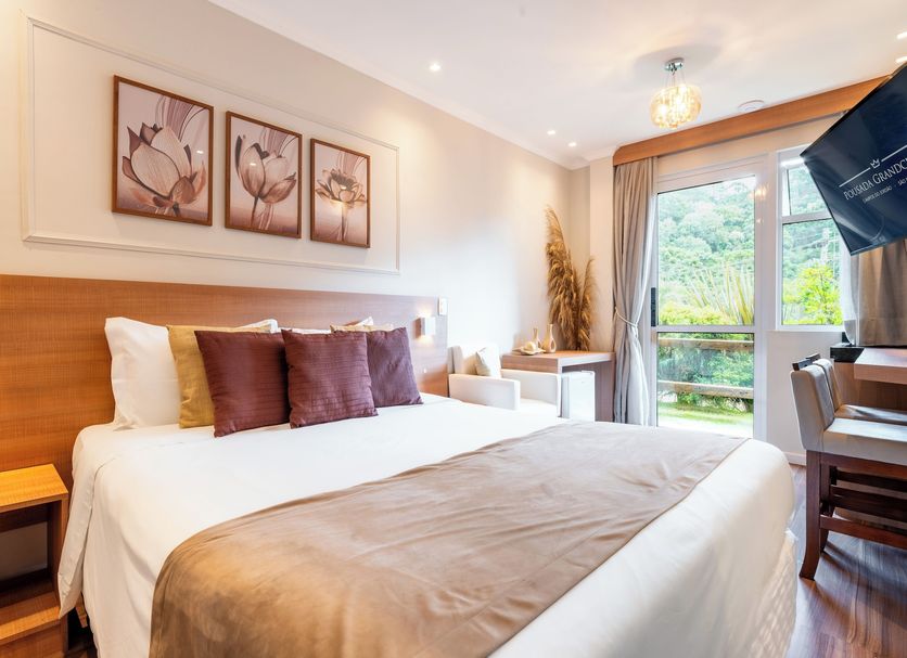 Pousada Grandchamp - Campos do Jordao guest room with king bed, window view, and desk in Campos do Jordão