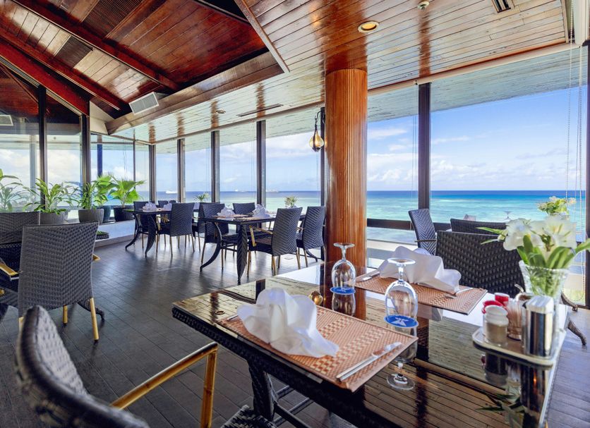 Grandvrio Resort Saipan in Garapan: oceanfront restaurant with tables and chairs beside large windows overlooking the sea.