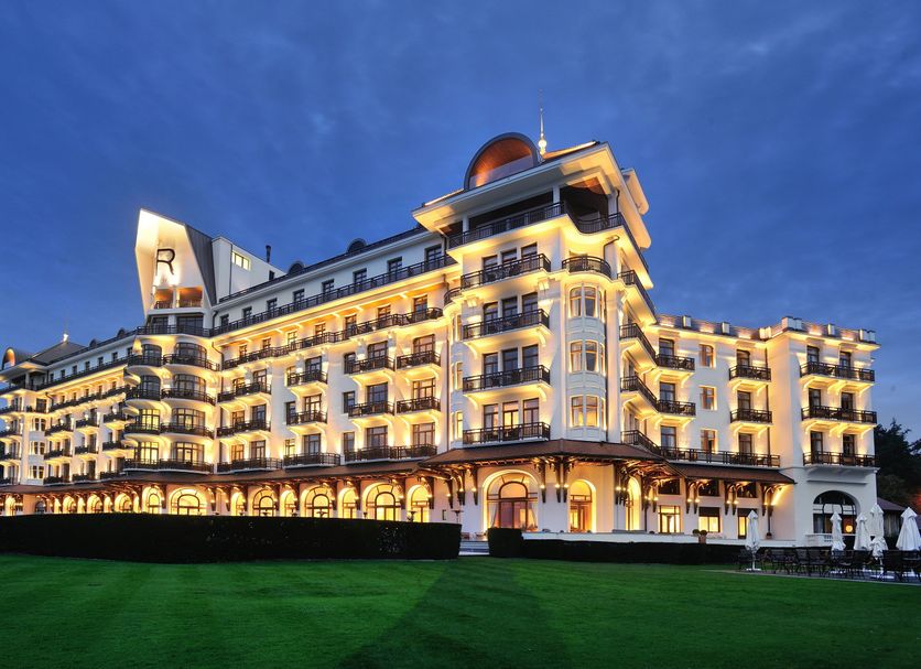 Hôtel Royal in Évian-les-Bains at dusk, showing a grand lit facade with balconies and arched lower levels.