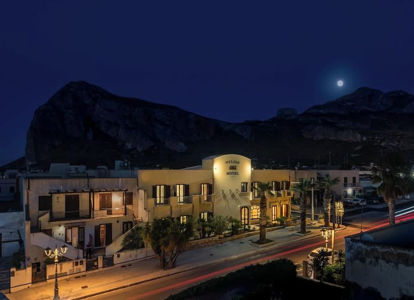 Helios Hotel in San Vito Lo Capo at night with illuminated facade and mountain backdrop