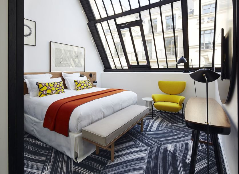 Hotel Du Ministere in Paris guest room with angled skylight windows, bed, desk, and yellow chair
