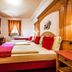 Chalet Mottolino, Livigno: cozy triple bedroom with wood-paneled headboard, red accents, and window curtains