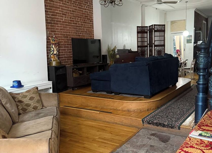 The Macaw Guesthouse in New York living area with raised wood floor, navy sofa, brick wall and staircase