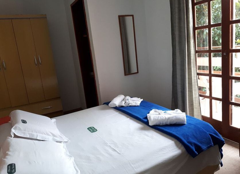 Pousada Ilha Morena in Florianopolis bedroom with a bed, wardrobe, mirror and balcony door to greenery.