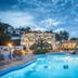Stafylos Suites & Boutique hotel in Stafylos with lit pool, palm trees, and hillside rooms at dusk