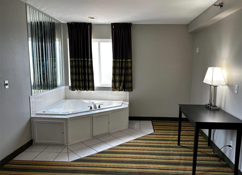 Super 8 by Wyndham Mound City room with corner jetted tub, table, lamp, and striped carpet