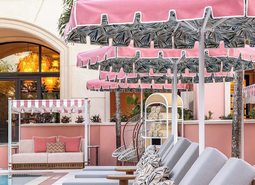 Palm House Hotel Palm Beach courtyard with pink cabanas, striped umbrellas, and poolside lounge chairs