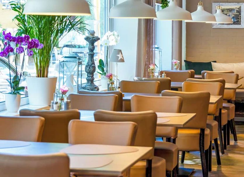 Auto-Parkhotel Hamburg St Pauli dining room with tables, tan chairs, pendant lights and potted plants