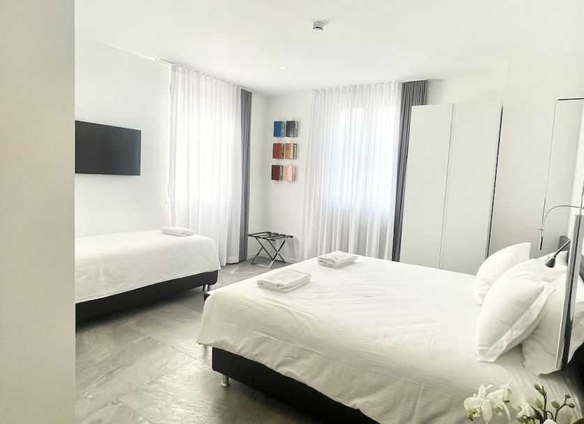 Le Muraine in Bergamo guest room with two beds, bright windows, and a wall-mounted TV