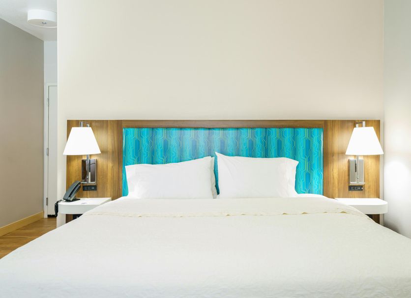 Hampton Inn Garden City guest room with king bed, white linens, wood headboard and bedside lamps