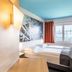 B&B Hotel München City-Ost room in Munich with colorful mural wall, twin bed, and window with red curtains