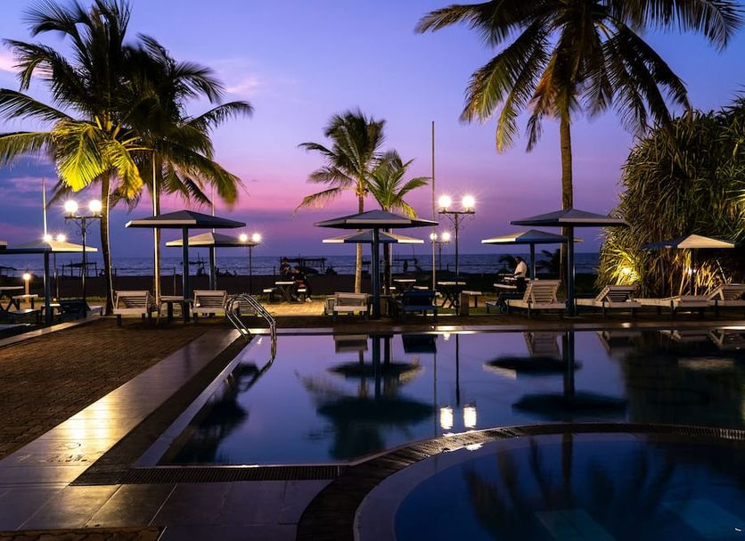 Rani Beach Resort in Negombo poolside at dusk with palm trees, lounge chairs and ocean view