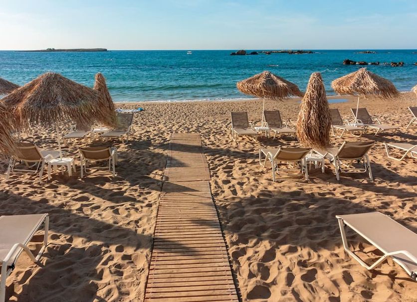 Christina Beach Hotel, Chania: sandy beach with sun loungers and straw umbrellas facing the sea