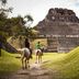 Ka'ana Resort in San Ignacio with horseback riders approaching a Mayan pyramid amid grassy ruins
