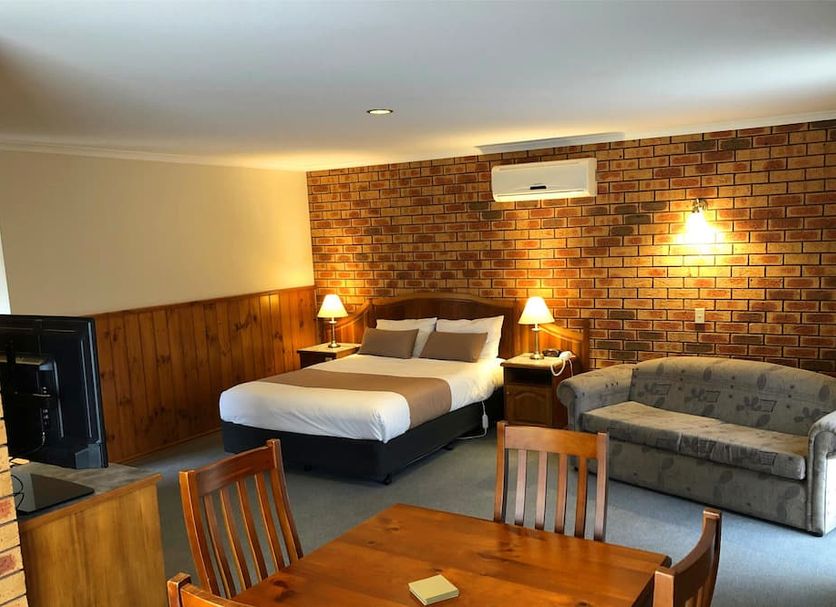 Victoriana Motor Inn Ballarat room with king bed, sofa, dining table, brick accent wall and lamp lighting