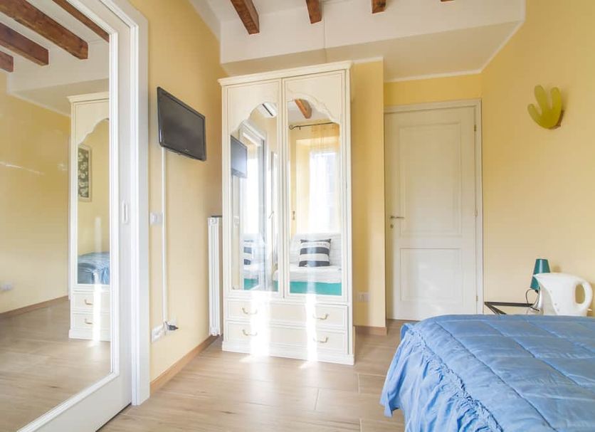 B&B Antico Cortile in Milan guest room with blue bedspread, wardrobe, wall-mounted TV and wood-beam ceiling