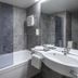 Achat Hotel Monschau bathroom with bathtub, glass shower screen, and wall-mounted sink in Monschau