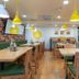 Bloom Hotel - Sg Highway in Ahmedabad dining area with wooden tables, green chairs and yellow pendant lights