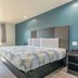 Studio 6 Suites Perris, CA guest room with king bed, desk, blue accent wall, and window view