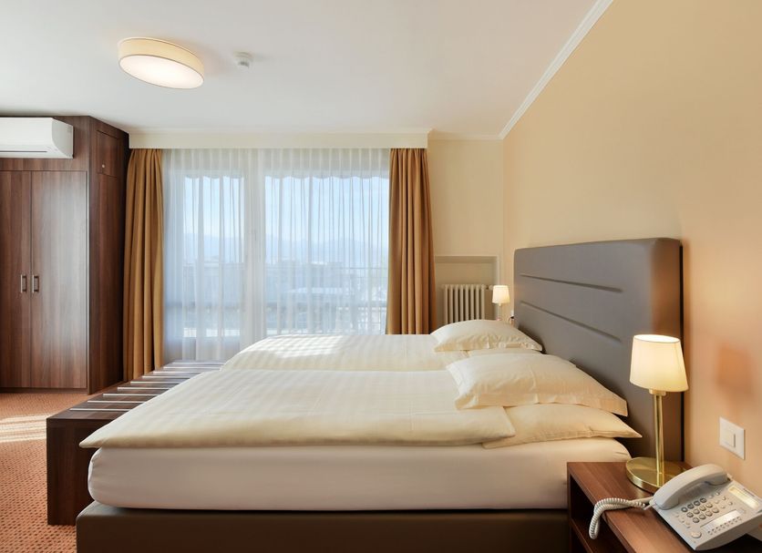 Hotel Elite Lausanne guest room with twin beds, wardrobe, and city view through large windows