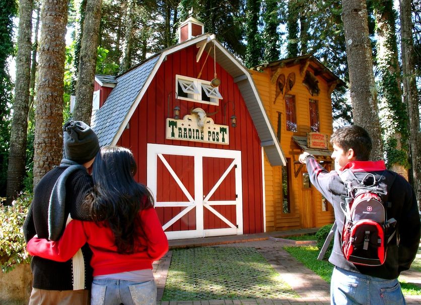 Canada Lodge in Campos do Jordão: red barn-style lodge among tall trees, with guests nearby