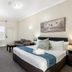 Sanctuary Resort Motor Inn in Coffs Harbour guest room with queen bed, sofa, TV, and window light