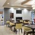 Comfort Suites Minot South lobby seating area with tables, chairs, fireplace and wall-mounted TV in Minot