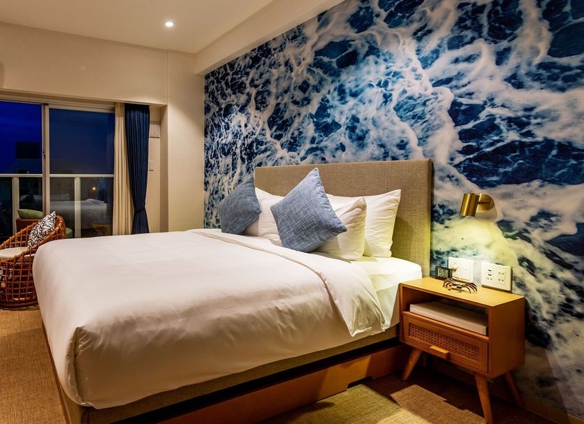 The Moana in Chatan guest room with double bed, woven chairs, balcony doors and ocean-inspired wall art