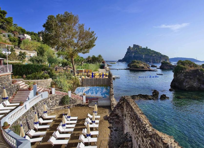 Strand Hotel Delfini in Ischia with seaside terrace, loungers, and rocky island views