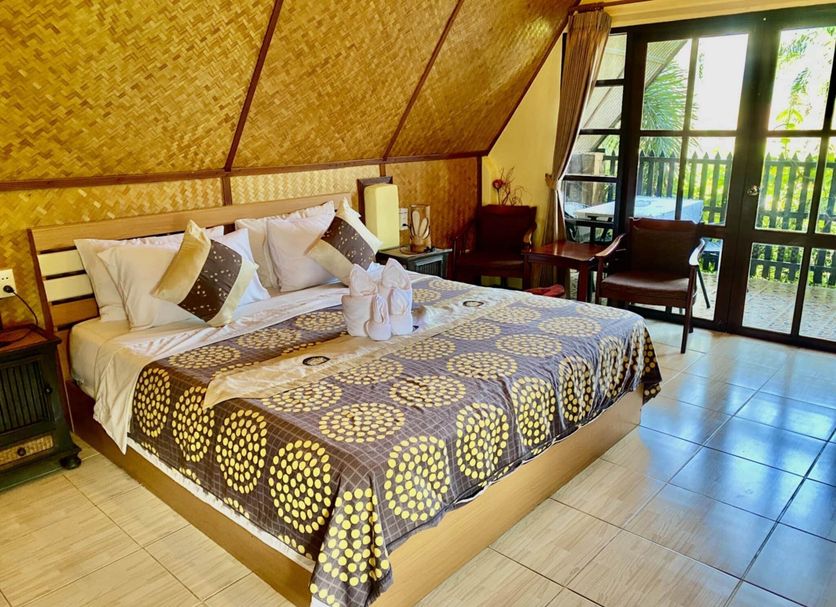 Homestay Chiangrai in Chiang Rai: thatched-roof bedroom with a king bed, balcony doors, and garden view
