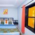 Sarges Hotel in Serrekunda guest room with double bed, bedside tables, and window with orange curtain