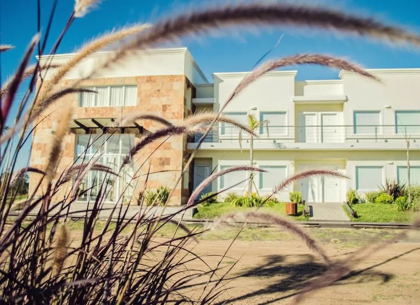 Tagüe hotel in Gualeguaychú, exterior with modern white facade and stone accents behind tall grasses.