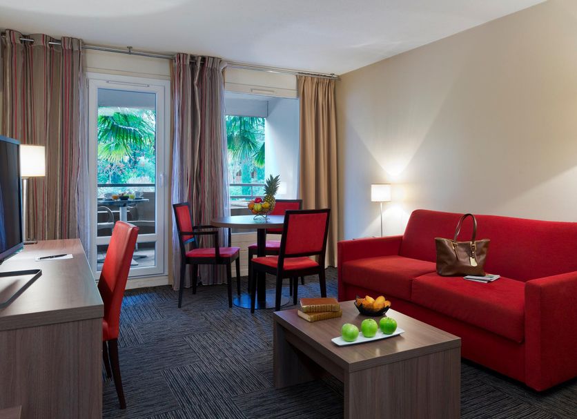Residence La Reserve Ferney-Voltaire room with red sofa, table, desk and balcony doors