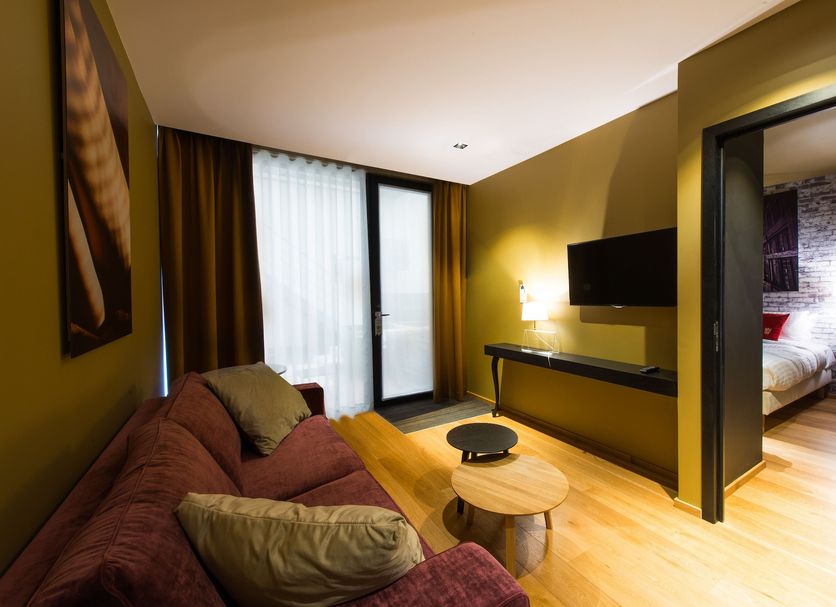 Hotel The Royal Snail in Namur guest room with sofa, wall-mounted TV, coffee tables, and balcony door