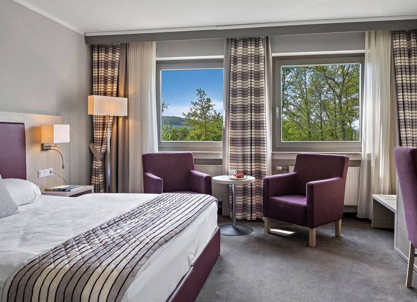 Hotel Diehlberg room in Olpe with bed, seating area, and large windows overlooking trees and water