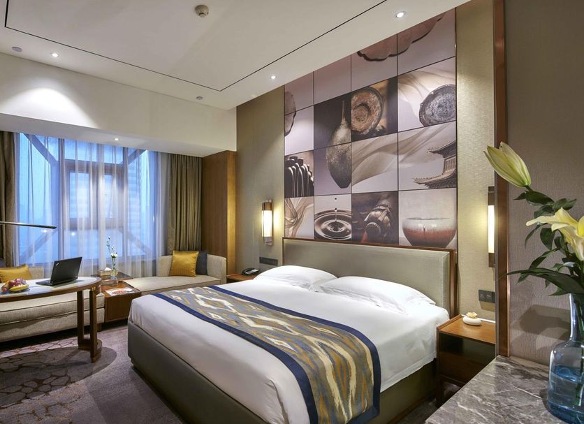 Henan Sky-Land Gdh Hotel in Zhengzhou guest room with king bed, sofa seating, and city-view window