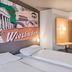 B&amp;b Hotel Wiesbaden-Ost room with twin beds, wall art, and wood-accented entry in Wiesbaden