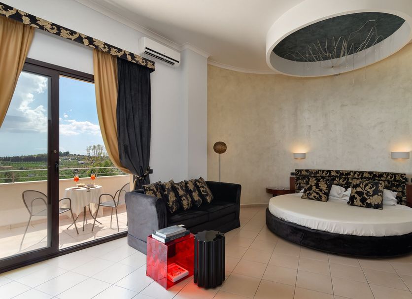 Grand Hotel Sofia, Noto: suite with round bed, sofa, balcony doors and countryside view