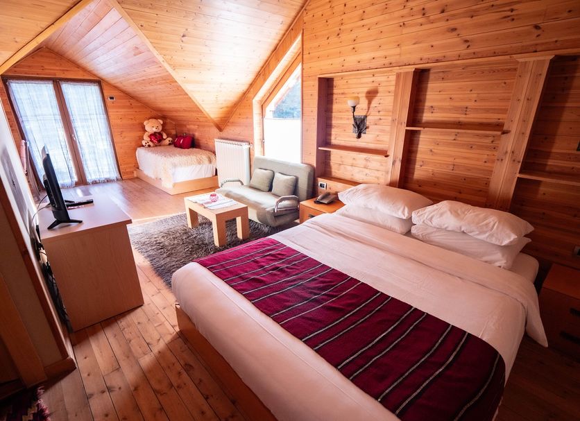 Natyral Razma Resort in Razem: wooden chalet room with two beds, sofa, TV and mountain window views
