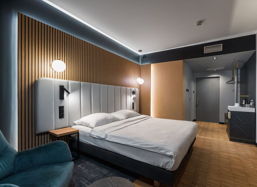 Artis Loft Hotel Mszczonów modern guest room with double bed, wood slat wall and teal chair