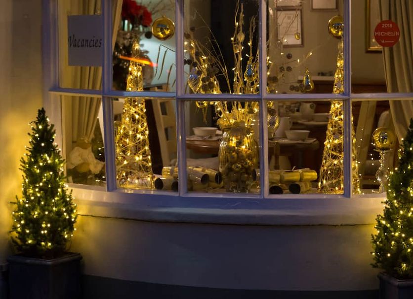 The Old Brewhouse in Cirencester, festive window display with lit Christmas trees and gold decorations