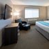 Paynesville Inn And Suites guest room with king bed, chair, wall-mounted TV and window in Paynesville